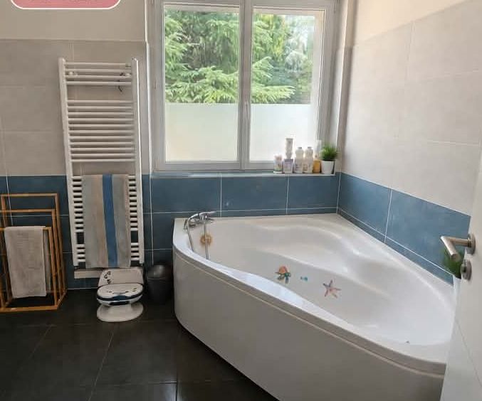 La même salle de bain dégagée : sèche-serviettes libéré, porte-serviettes en bois installé, produits regroupés sur le rebord et plante verte