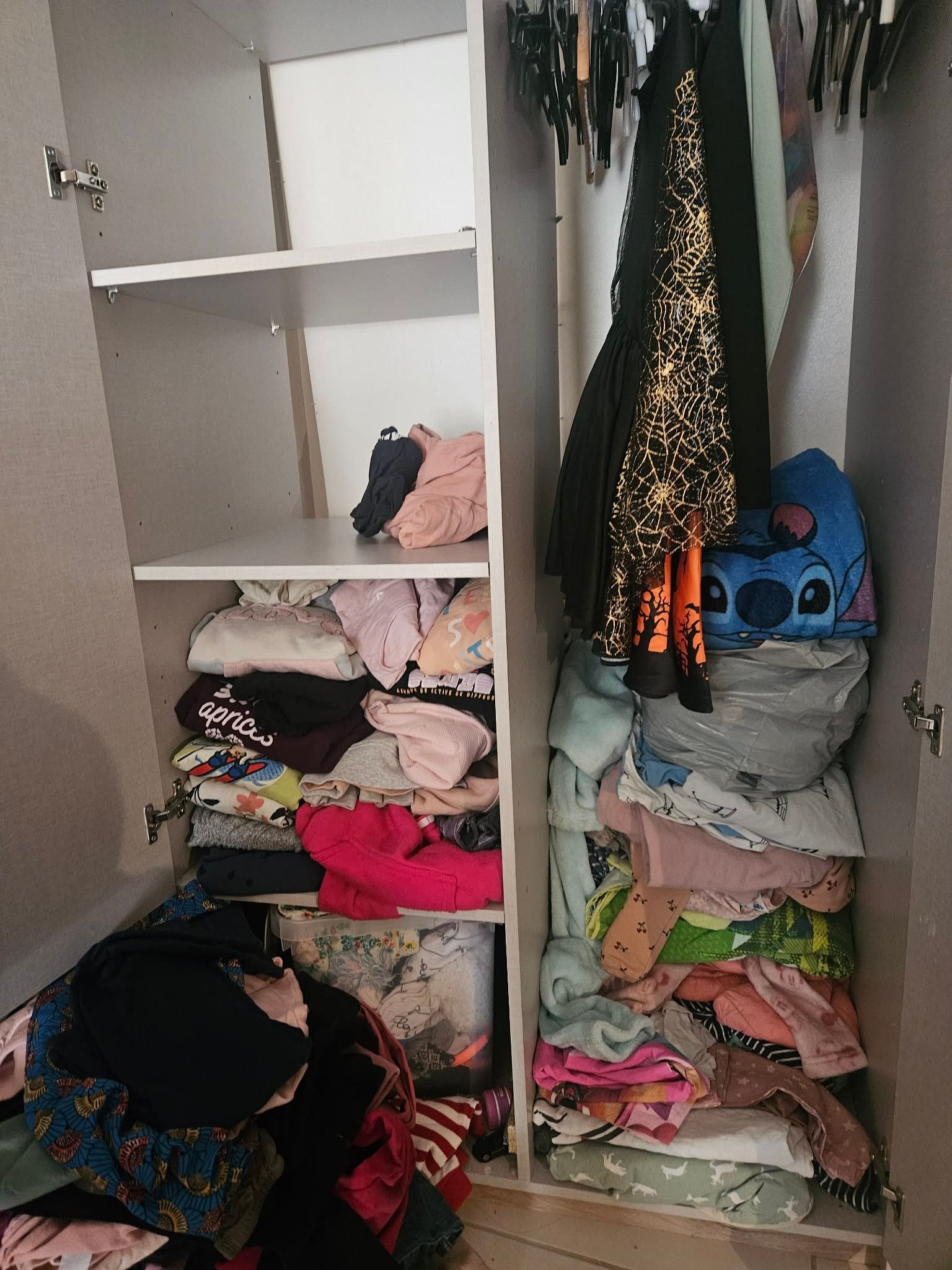 Placard d'enfant dont les étagères débordent de vêtements empilés en vrac, avec un tas de linge posé au sol devant la porte ouverte