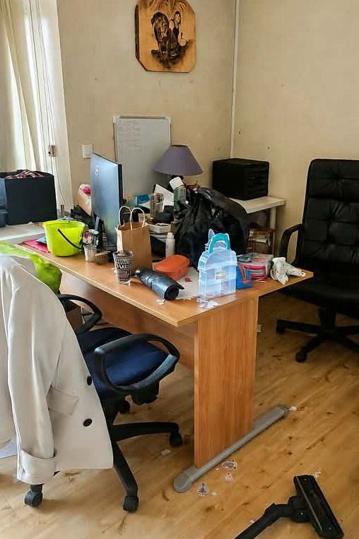 Bureau couvert d'objets, de sacs et de papiers, manteau posé sur la chaise, aspirateur et déchets au sol