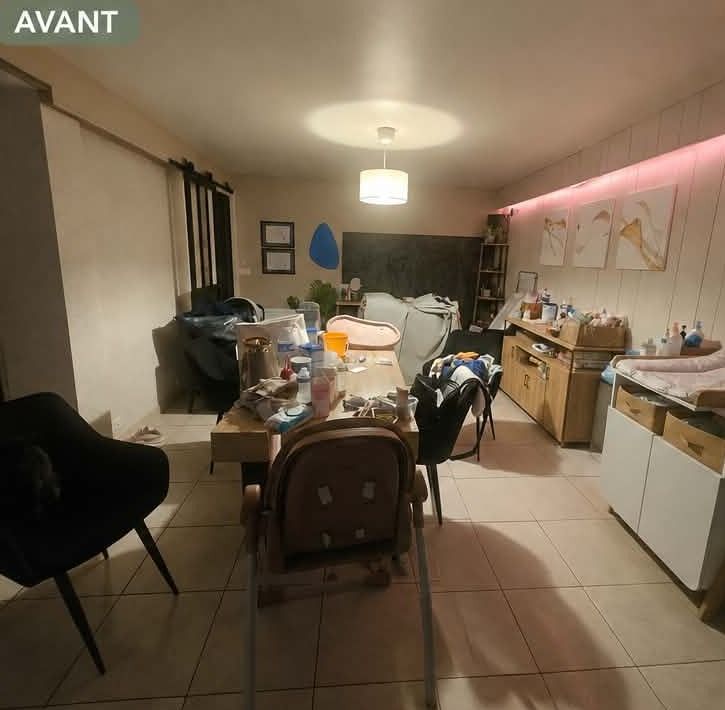 Salle à manger dont la table disparaît sous les objets, avec du matériel de puériculture et des cartons occupant le passage