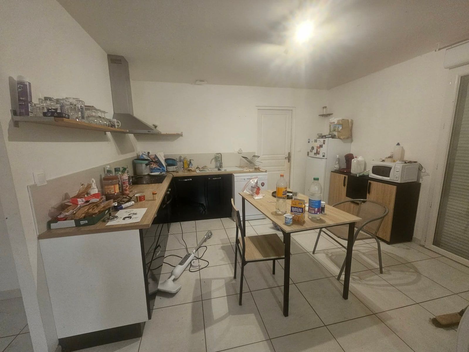 Cuisine dont les plans de travail sont couverts d'ustensiles, de provisions et de vaisselle, avec une table encombrée au centre
